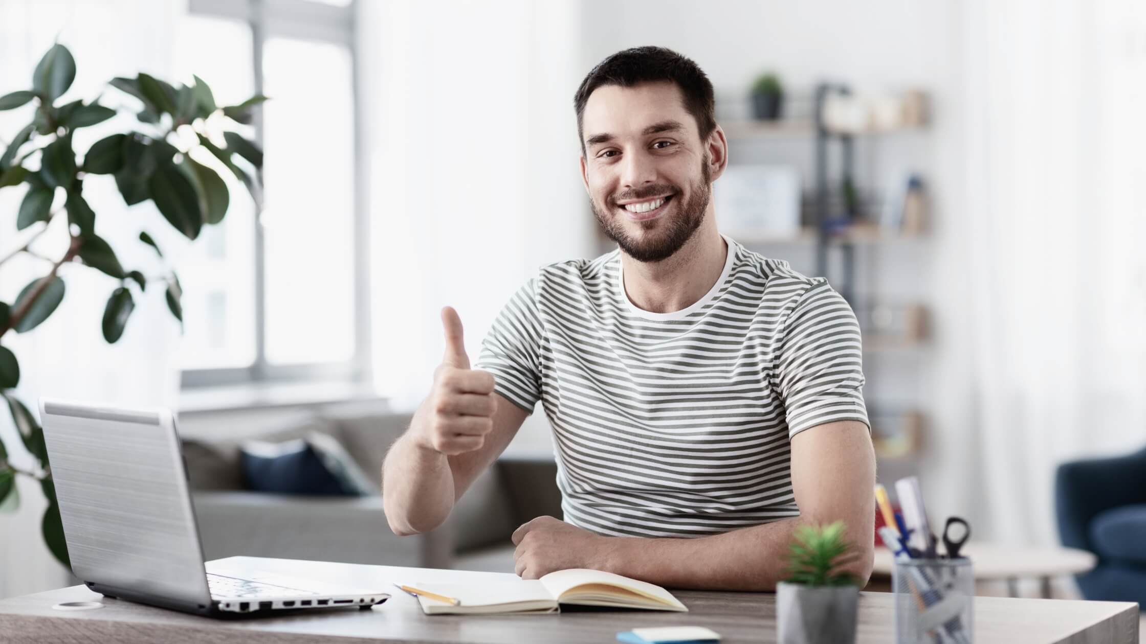 Hombre sonriendo, sentado en su espacio de trabajo con una computadora portátil y dando un pulgar hacia arriba, simbolizando satisfacción y aprobación de los servicios de ChatGPT sin necesidad de registro